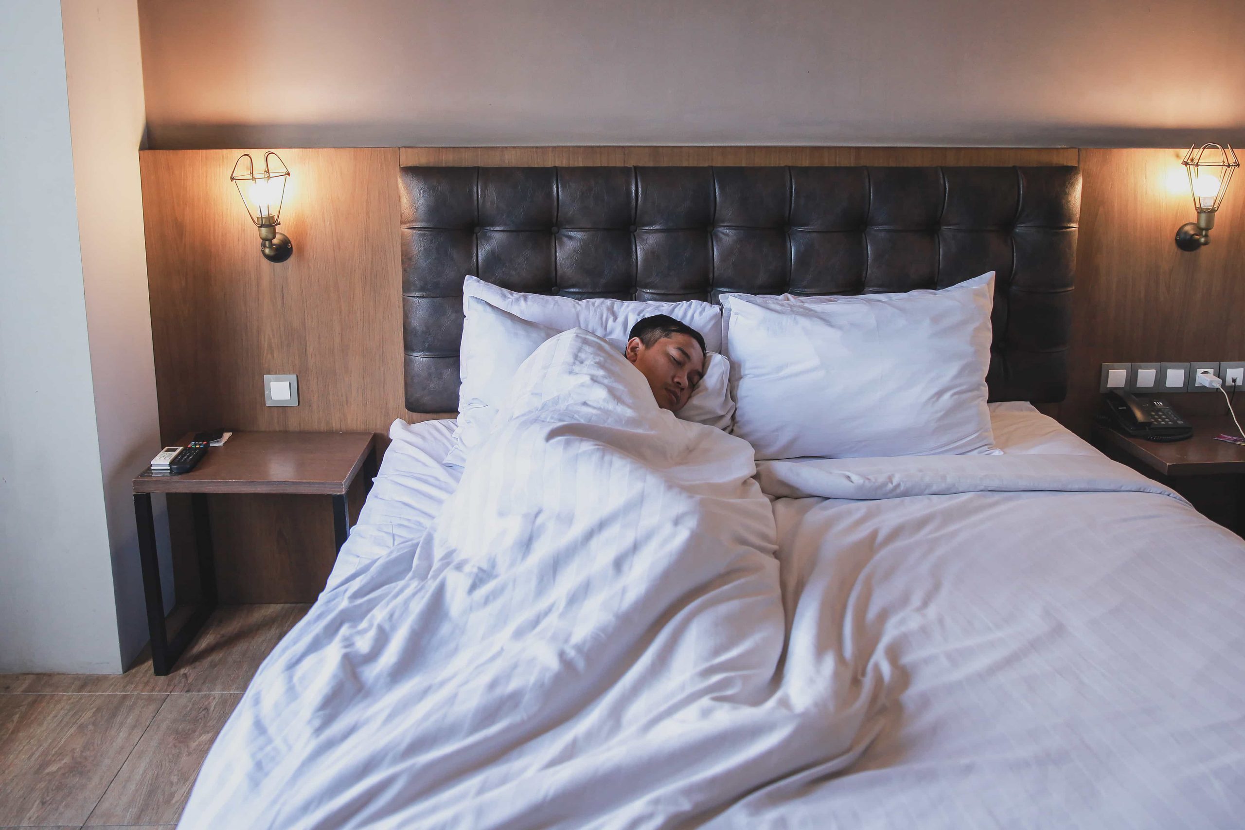 Mężczyzna śpiący w łóżku przykryty pościelą.