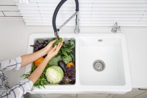 Kobieta myje warzywa w zlewozmywaku ceramicznym